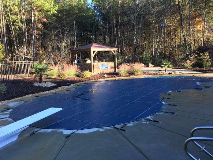 A pool fitted with a dark blue safety cover beside a pavilion and a black metal fence