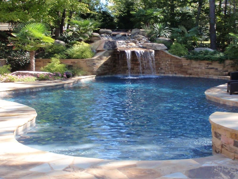 A backyard pool with a small waterfall and stone wall