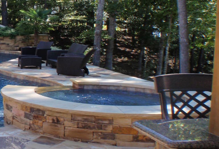 A stone-walled spa beside a pool with outdoor seating
